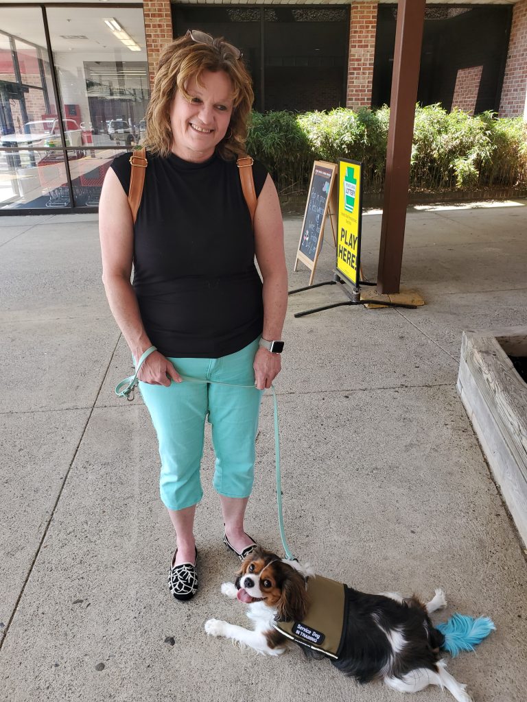 Woman in bright azul trousers training a service dog with a matching blue dyed tail